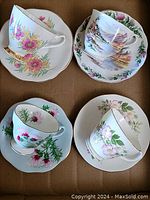 Four assorted vintage teacups and matching saucers with floral patterns and gold trim displayed in a box.