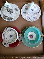 Overview of all four cups and saucers laid out in a cardboard box showing different floral designs and shapes.