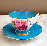 Side view of the Aynsley teacup and saucer set showing pink rose exterior and turquoise interior with gold trim