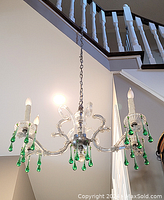 Full view of a 4-light chandelier suspended from a chain under a staircase, showing clear arms and green glass drops