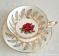 Top view of porcelain cup and saucer showing red rose and surrounding gold leaf design, scalloped edges with gold trim
