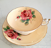 Front view of cup resting inside matching saucer showing pink rose design and scalloped gold edges.