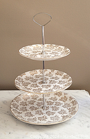 Front view of the three-tier porcelain dessert stand showing gold floral pattern on plates and metal handle.