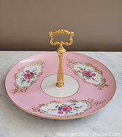 Top view showing pink porcelain surface decorated with floral and gold details and gold ornate handle in center.