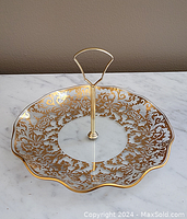 Side angle view of the gold leaf patterned glass dessert stand showing clear scalloped edges and gold handle.