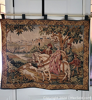 Full view of the tapestry hanging, showing the medieval scene with riders and castle.