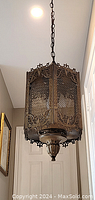 View of octagonal metal pendant light highlighting detailed scrollwork and mesh metal panels with gold-tone finish.