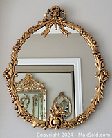 Full view of oval brass framed wall mirror reflecting other mirrors.