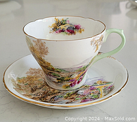 Cup and saucer with colorful scenic landscape, showing gold trim and pale green handle on cup.
