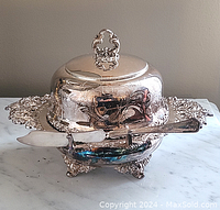Assembled silver-plated butter dish set with cover, base, glass liner, and butter spreader on marble surface