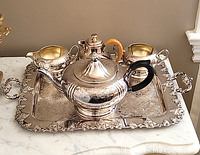 Silver plated tea set on tray on marble surface showing teapot, sugar bowl, creamer, coffee pot, and serving tray with ornate leaf border.
