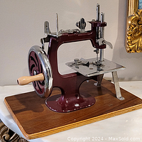 Side view showing the burgundy metal frame, wooden handle, and metal sewing plate mounted on wood base.