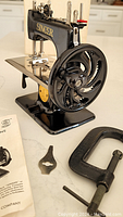 Front angle of black enamel Singer machine on table with instruction manual, wrench and C-clamp laid out
