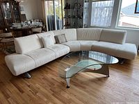 Wide angle front view of the curved beige sofa with rounded armrest and legs, shows overall shape and upholstery.
