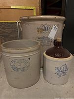 Three antique stoneware items: a large Monmouth Pottery Co. crock, a medium Western Stoneware crock, and a small Western Stoneware jug with cork.