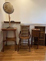 Photo showing the antique globe on a tall stand, the small wooden side table with wheels, the wooden chair with glued damage, a small wooden cabinet, and two wooden letterbox trays leaning against the wall.