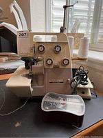 Front-left angle view showing threading dials, spool holder, bobbin case, and power cord.