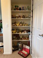 Closet with multiple shelves holding an assortment of vintage glassware, ceramics, and decorative household items.