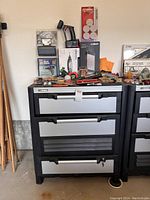 Full view of the Husky 3 drawer garage cabinet with many tools and boxes arranged on top and in front of it.