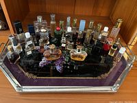 Top-down photo showing a collection of miniature perfume bottles on a rectangular mirrored tray with a purple decorative background, arranged in multiple rows.