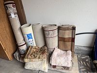 Photo showing multiple rolled and folded area rugs and mats in various colors and patterns.