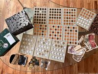Top view of coins placed on coin holding pages along with foreign currency bills and coin albums on glass table.