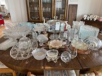 Full lot view showing a large assortment of vintage crystal serving platters, bowls, snack sets, and one clock arranged on a wooden dining table.