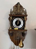 Full view of vintage Dutch chiming wall clock with brass pendulum and ornate wood and brass decoration.
