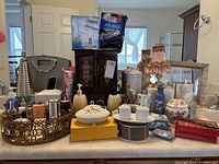 Wide view of collection of bathroom and vanity items including vintage perfume bottles, powder compacts, soap dispensers, boxed bath products and more arranged on vanity counter.