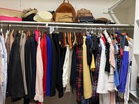Closet rod with assorted women's clothing hung on hangers including tops, sweaters, coats, and dresses in neutral and bright colors.
