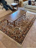 Top view of the 5x7 wool rug showing the floral and geometric pattern, with a wooden table on top and a beige carpet floor surrounding it.
