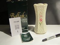 Full view of Belleek vase next to original green box and booklet with a pen for scale