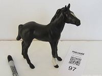Black ceramic horse figurine standing on all four legs with one white hoof, viewed from the front and right side.