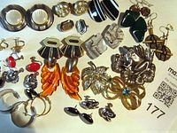 Full lot view showing a variety of costume jewelry earrings and brooches laid out on white background.