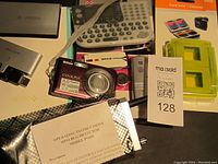 Photo of the Nikon Coolpix digital camera, mini bug detector with instruction manual, label maker keyboard, and various electronic accessories including unopened items.