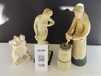 Three vintage signed figurines including a nude figure, a group of three dancing figures, and a woman churning butter.