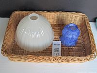 Two glass shades and one rectangular wicker basket shown together. The white semi-opaque glass shade has ribbed texture and the blue shade is marbled and bulbous. The basket is woven natural brown.