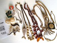 Photo of assorted vintage costume jewelry items laid out on white background showing necklaces, brooches, pins, and earrings