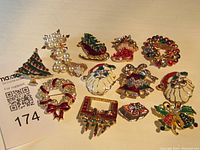 Full collection of 13 vintage Christmas brooches arranged flat on a surface showing different holiday-themed designs including tree, sleigh, wreath, boot, Santas, bells, gift box, and pearl holly leaves.