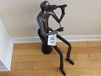 Front side view of the cast metal violin player figurine sitting on black metal stool.