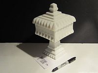 Front view of vintage white milk glass bonbon box with lid and pedestal base, pen for scale.