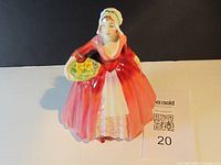 Front view of Royal Doulton porcelain lady figurine in red dress holding basket of yellow flowers.