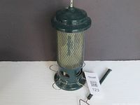 Full view of the Squirrel Buster bird feeder showing the metal base, mesh tube, and detached metal hook handle laying beside it.