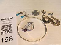 Photo showing all jewelry pieces: turquoise blue drop earrings (costume jewelry), iron cross pin 925 Mexico, sterling silver ring with purple stones, sterling silver bangle, sterling silver hoop earrings.