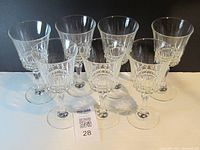 Seven clear cut crystal wine glasses arranged with identification tag visible.