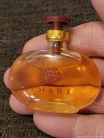 Front view of Imari perfume bottle held in hand, showing amber perfume and brand name with floral emblem.