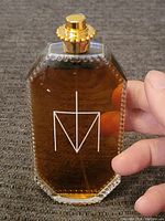 Front view of the perfume bottle showing amber liquid and logo.