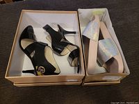 Both pairs of shoes in their boxes, black heels on left, nude flat sandals with iridescent straps on right