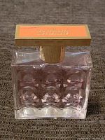 Front view of nearly full, textured glass perfume bottle with a gold and orange cap.