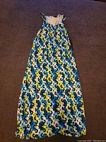 Full length image of sleeveless floral patterned dress laid flat on dark background, showing entire garment length and pattern details.